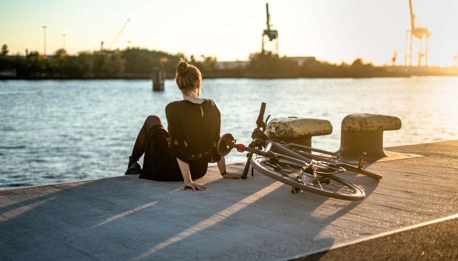 Eine junge Frau sitzt an der Hafenkante, das Fahrrad liegt daneben.